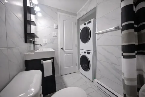Bathroom with sink and stacked laundry appliances — Rehoboth 1BR in Laval